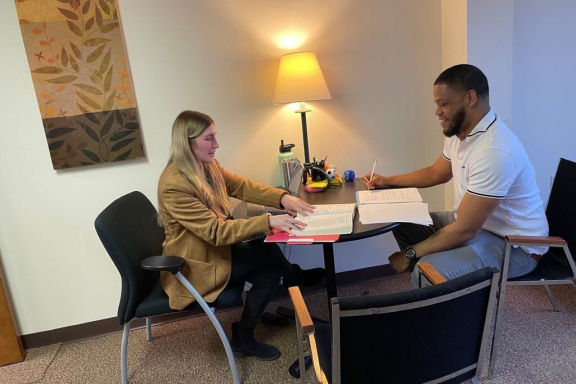 A light skinned person with long blond hair and dark skinned person with short dark hair work together at a table.
