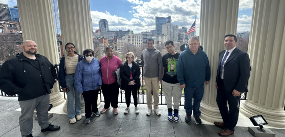 Group of nine adults smiling outdoors at the State House