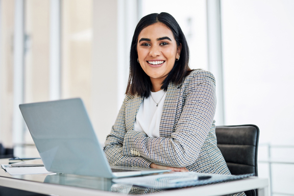 Young adult woman smiling sitting at a desk with a laptop.
