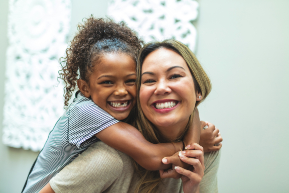A mom giving a young child a piggyback ride. They're smiling.