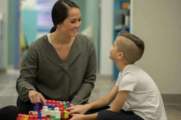 Behavior therapist and child seated on the ground indoors, smiling at each other 