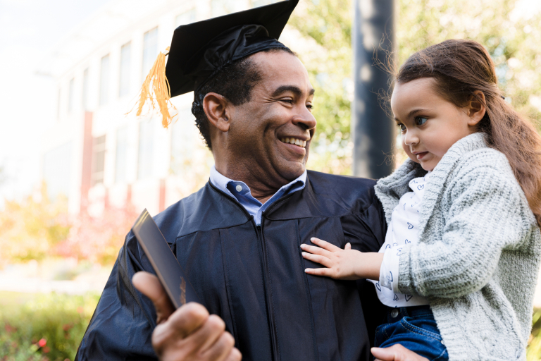 A middle-aged adult with short hair holds a child at graduation