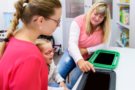 Two adults work with a young child on a tablet