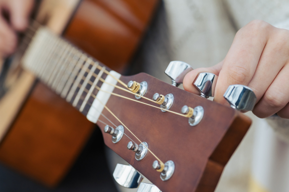 Light-skinned hand tuning an acoustic guitar