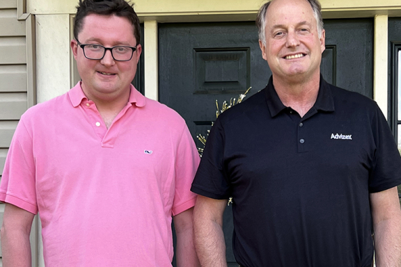Jack, a young adult man, and his dad smiling in front of their home.