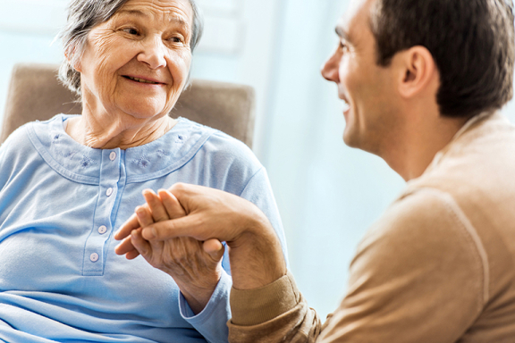 A senior-aged woman holding her adult son's hand