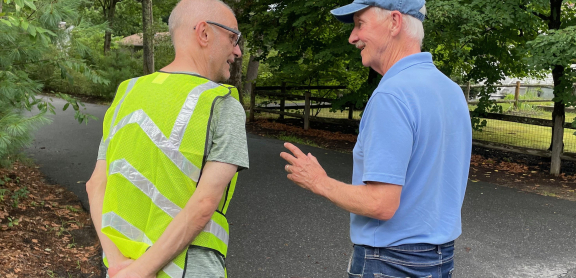 Two older men smiling and walking along a wooded road
