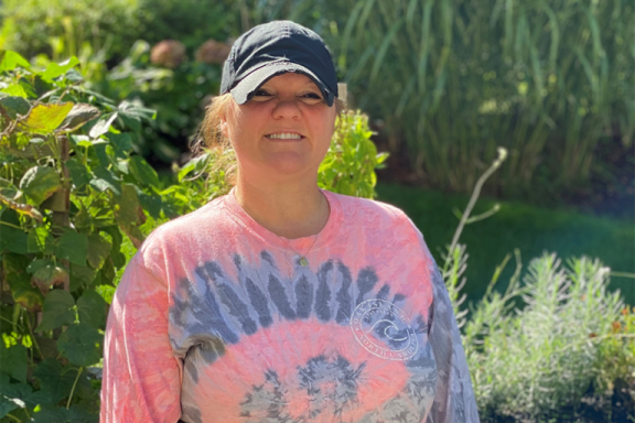 Amanda St. Amant smiling outside. She is wearing a hat and tie dye t-shirt.