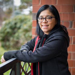 A woman smiling at the camera resting against a fence