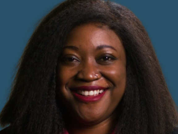 Adult with long dark hair and dark skin smiles at the camera