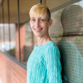 A young person leaning against the outside of a window and smiling